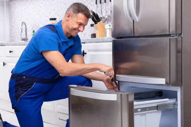 Mature Male Serviceman Repairing Refrigerator With Toolbox In  Kitchen